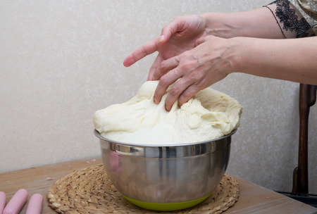 Kneading dough in the home kitchen for making sausages in the dough - close-up of female hands....