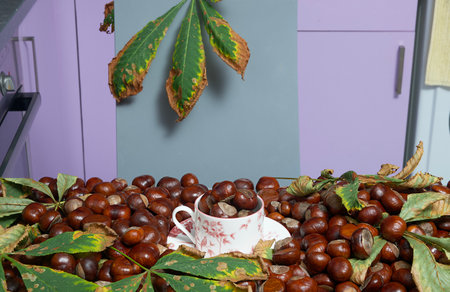 A tea bowl filled with chestnuts sits in the center of a table covered with lots of chestnuts and fallen autumn chestnut leaves. Photo of autumn mood in the home kitchen.の写真素材