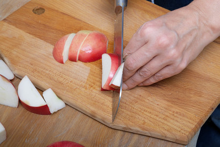 Female hands cut a ripe red apple into small pieces in the process of making an apple pie in a home kitchen.の写真素材