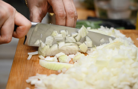 A woman holds a large sharp knife in her hand and cuts the onion into small pieces.の写真素材