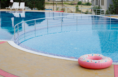 A large pool filled with clear clean water at the edge of which lies a beautiful brightly colored inflatable swimming lap. The atmosphere of calm relaxation on a sunny, serene day.の写真素材