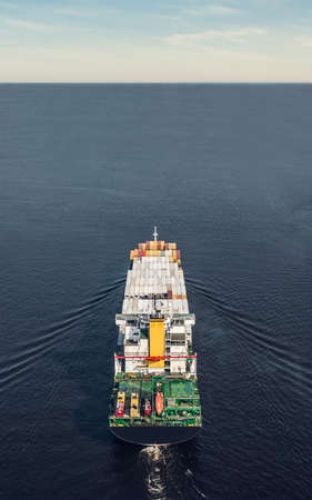 Back view of container ship floating in the sea. Vertical photography