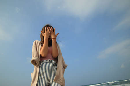 The girl against the blue sky covered her face with her hands. High quality photoの写真素材