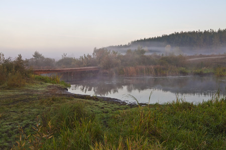 Wooden bridge over a small river in the mist at sunriseの写真素材