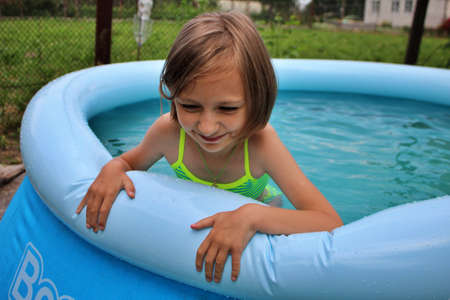 beautiful little girl in a bathing suit swims in a small blue pool
