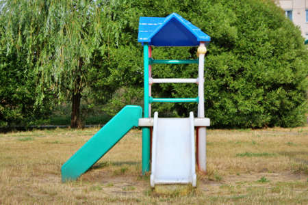 against the backdrop of green bushes, a plastic small children's playground with two slides