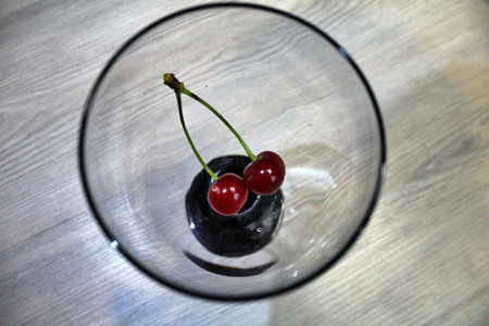 two bright red cherries on a branch at the bottom of the glass