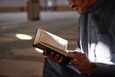 Portrait of a young Muslim male reading the Quran inside a mosque