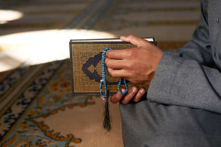 Hands holding prayer beads and the Quran in a mosque with sunlight