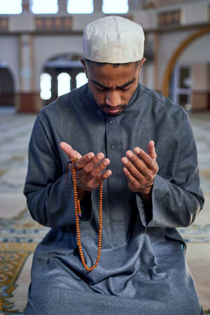 Muslim man praying in a mosque on his knees with prayer beadsの写真素材