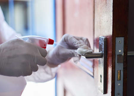 A cleaning professional sprays sanitiser onto a door handle