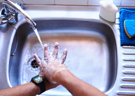 Overhead shot of an adult man washing his hands in the kitchen sink