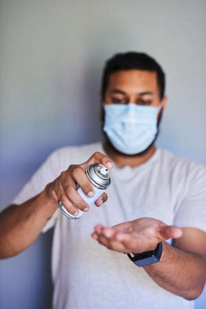 A young man spraying hand sanitiser onto his palmの写真素材