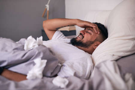 A sick man in bed holding his temples in pain from congestionの写真素材