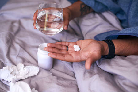 A close up of hands holding pills to treat flu or sickness in bedの写真素材