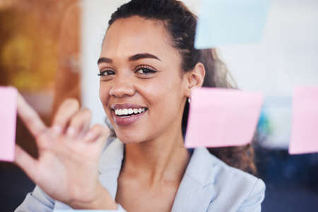 A young woman brainstorms ideas on sticky notes seen through window