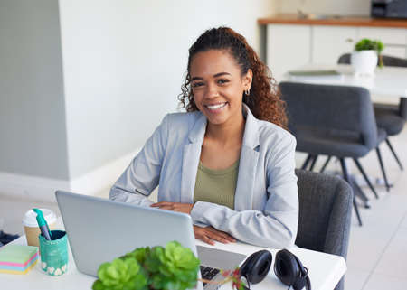 A young woman sits at her desk in a corporate office in front of her laptop
