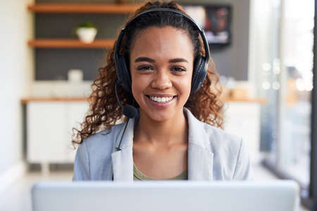 A centred view of a young woman behind her laptop with headset in modern office