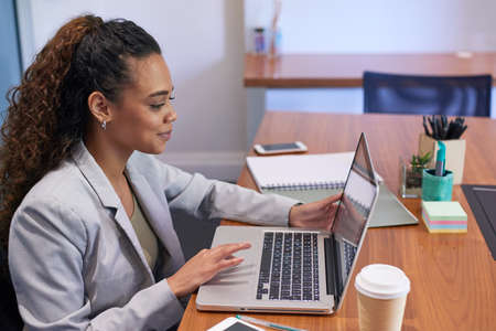 A young woman sits at her desk in a corporate office in front of her laptop