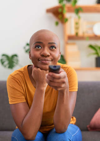 A young woman points the remote at the TV sitting on the sofa relaxing