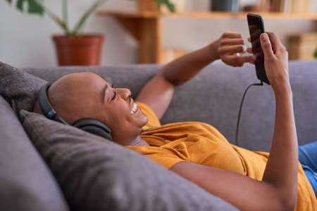 A young woman listens to music with headphones on the sofa in the living roomの写真素材