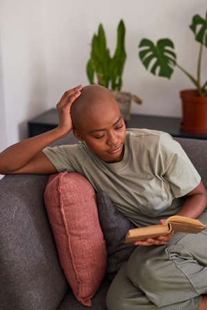 A young woman reads a novel at home on the couch