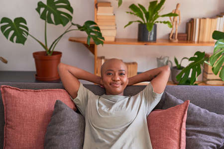 A young woman looks directly at the camera sitting on the couch at home