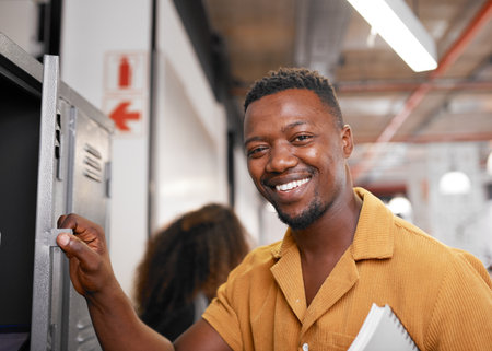 A young black student smiles at the camera and opens his locker on campusの写真素材