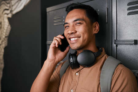 A young South East Asian man talks on the phone in front of campus lockersの写真素材