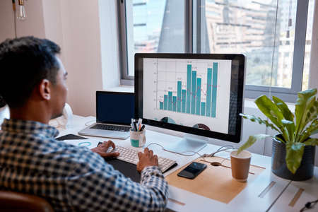 Side view of a businessman looking at a screen with graphs in front of cityscapeの写真素材