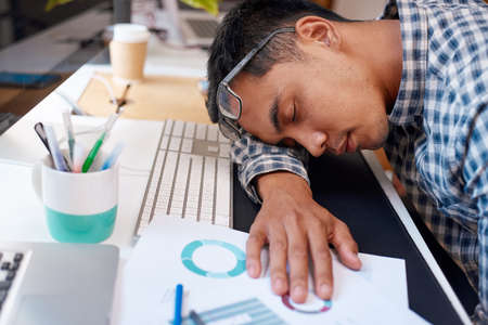 An exhausted businessman falls asleep at his desk with his workの写真素材