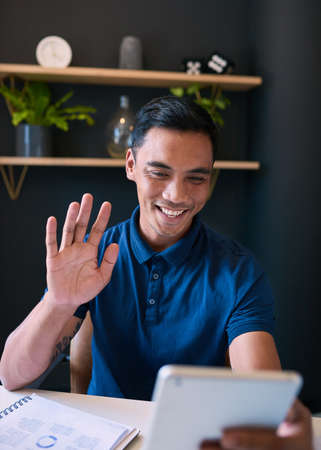 A young Asian man waves to a colleague on a digital tablet in the officeの写真素材