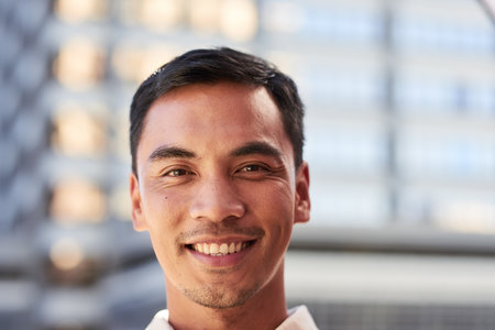 An attractive South East Asian man smiles for a portrait outside city buildingの写真素材