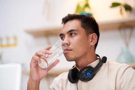 A sick Asian man drinks an effervescent flu tablet in water at work at his deskの写真素材