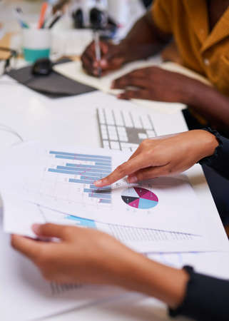 A close up of hands pointing to colourful graph with another person taking notes
