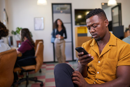A man scrolls on his cellphone looking bored at work in the busy office