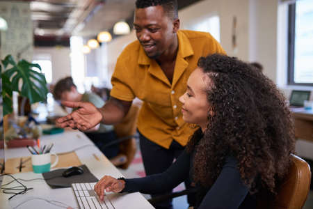 A young woman looks at her screen while her coworker gives advice