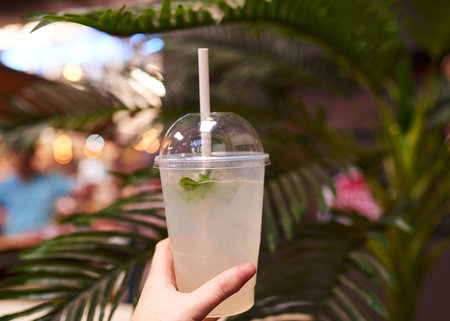 A white woman holds a takeaway lemonade at a summer market with palm treeの写真素材
