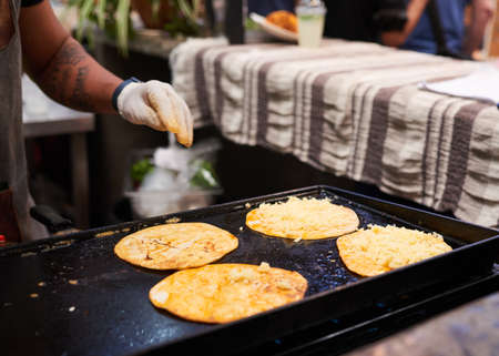 A man sprinkles cheese on a soft shell taco at a market - close up