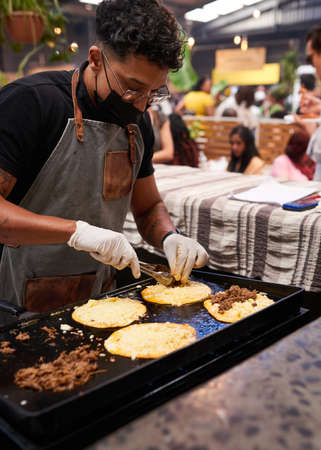 A chef spoons pulled beef onto tacos on the grill at a busy food marketの写真素材