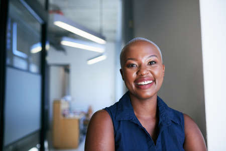 A young attractive Black woman smiles in the office corridor