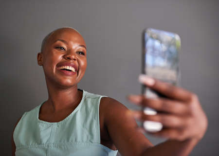 A young Black woman takes a selfie with grey backgroundの写真素材