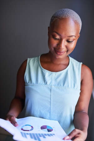 A young Black businesswoman reads a financial report with charts and graphsの写真素材