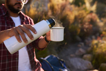A man pours hot water from a flask into his coffee mug while backpacking camping