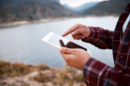A close up of hands swiping on a tablet with lake and mountainsの写真素材