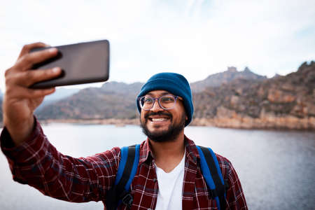 A happy hiker takes a selfie using smartphone with lake and mountainsの写真素材