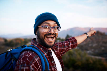 An excited backpacker points to the mountain view behind him on hiking tripの写真素材
