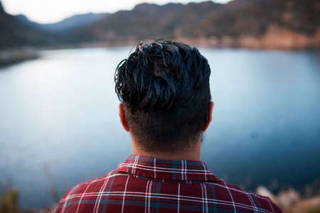 The back of a mans head while he admires the lake view on camping mountain tripの写真素材