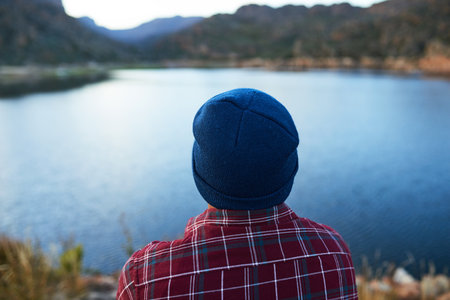 The back of a mans head while he admires the lake view on camping mountain tripの写真素材