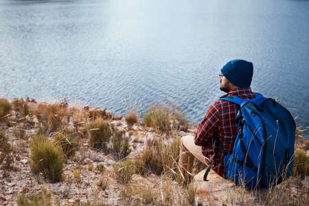 A backpacker takes a break and sits on a rock by the lake while hikingの写真素材